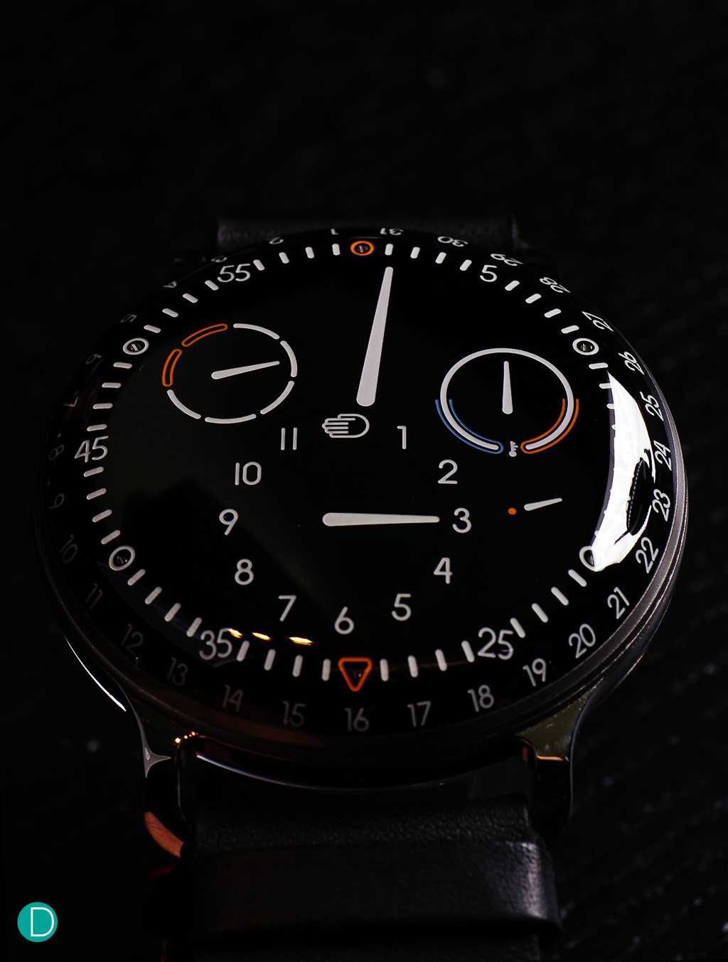 Ressence New Type 3. The hours are indicated by the subdial at 6 o'clock. Below that, shown by a small orange triangle is the date. The minutes by the large central hand. At 10 o'clock is the Day indicator, weekends marked in orange. The subdial at 2 o'clock is the new oil temperature indicator. Below that is the seconds hand.