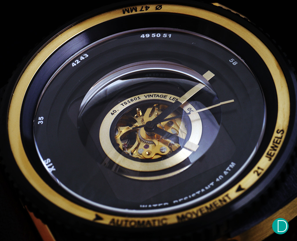 The dial is a 3 layer construction in black and gold, with what seems to be a multi layer sapphire crystal which is made to look like the elements of a lens as one looks down the barrel.
